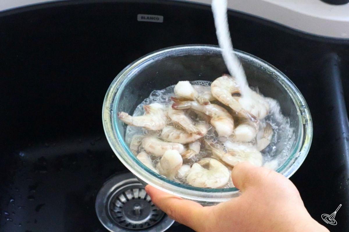 Someone rinsing raw shrimp under cold water.