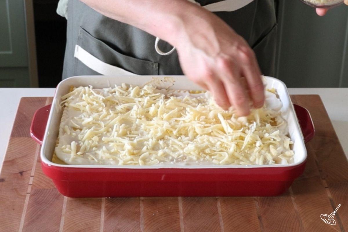 Someone sprinkling grated mozzarella on top of lasagna. 