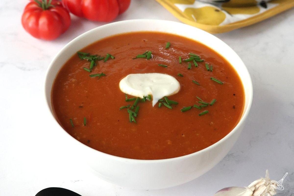A white bowl of roasted tomato and garlic soup with garnish. 