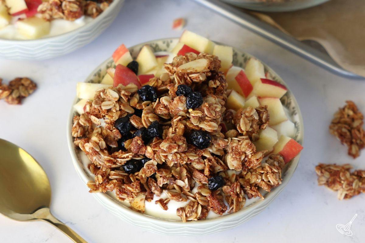 Blueberry Flax Granola in a bowl over yogurt with diced apples.