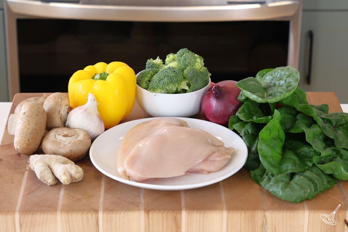 Ingredients on a cutting board, including chicken bread, swiss chard, and other vegetables. 