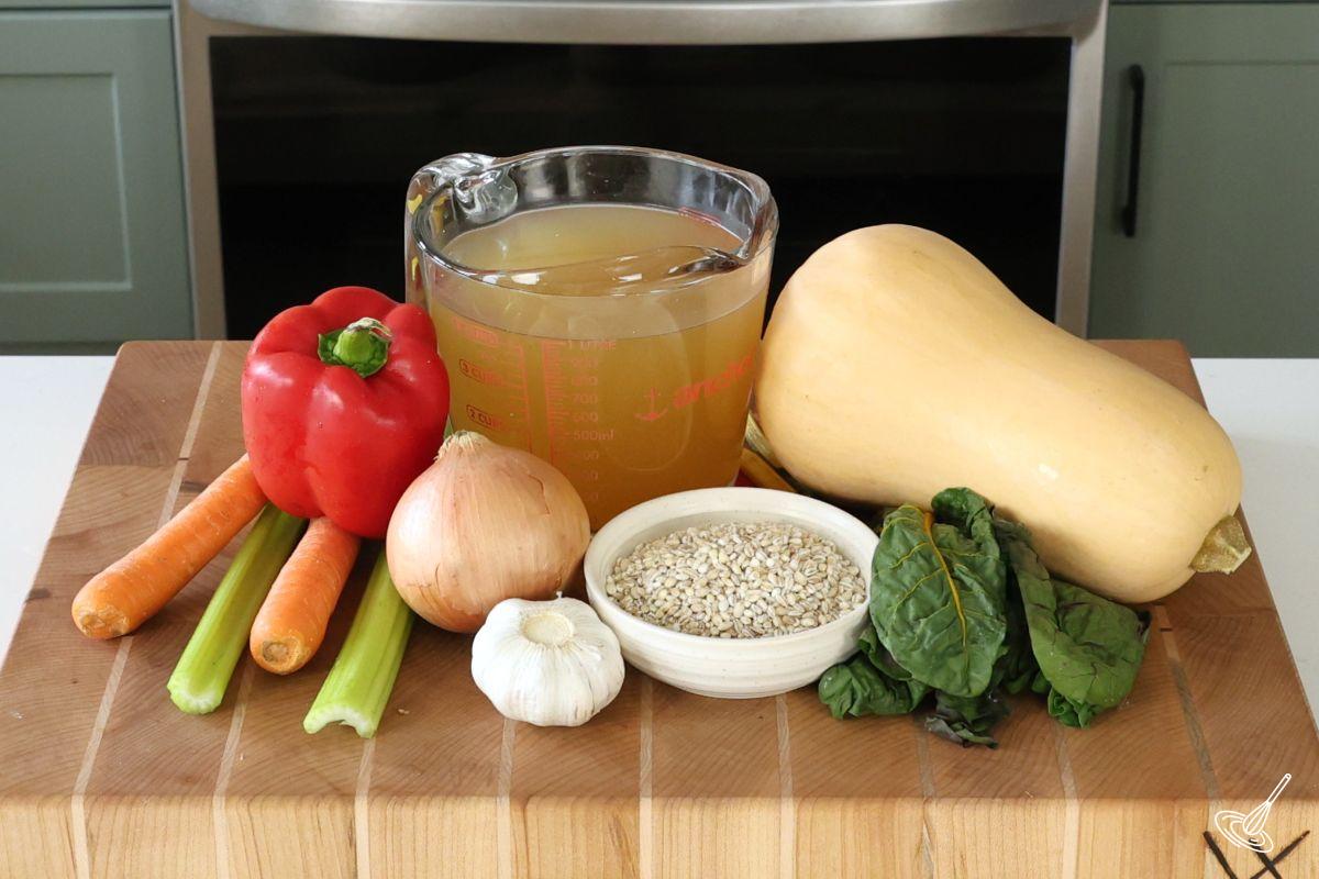Ingredients on a cutting board, including carrots, celery, butternut squash, and chicken broth. 