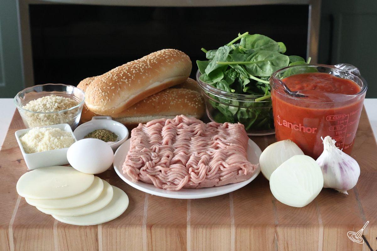 Ingredients on a cutting board, including ground turkey, spinach, tomato sauce and parmesan. 