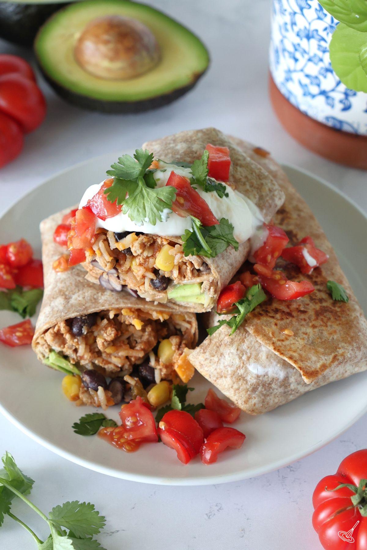 Ground Turkey Burritos stacked on a plate and garnished with sour cream and dice tomatoes. 