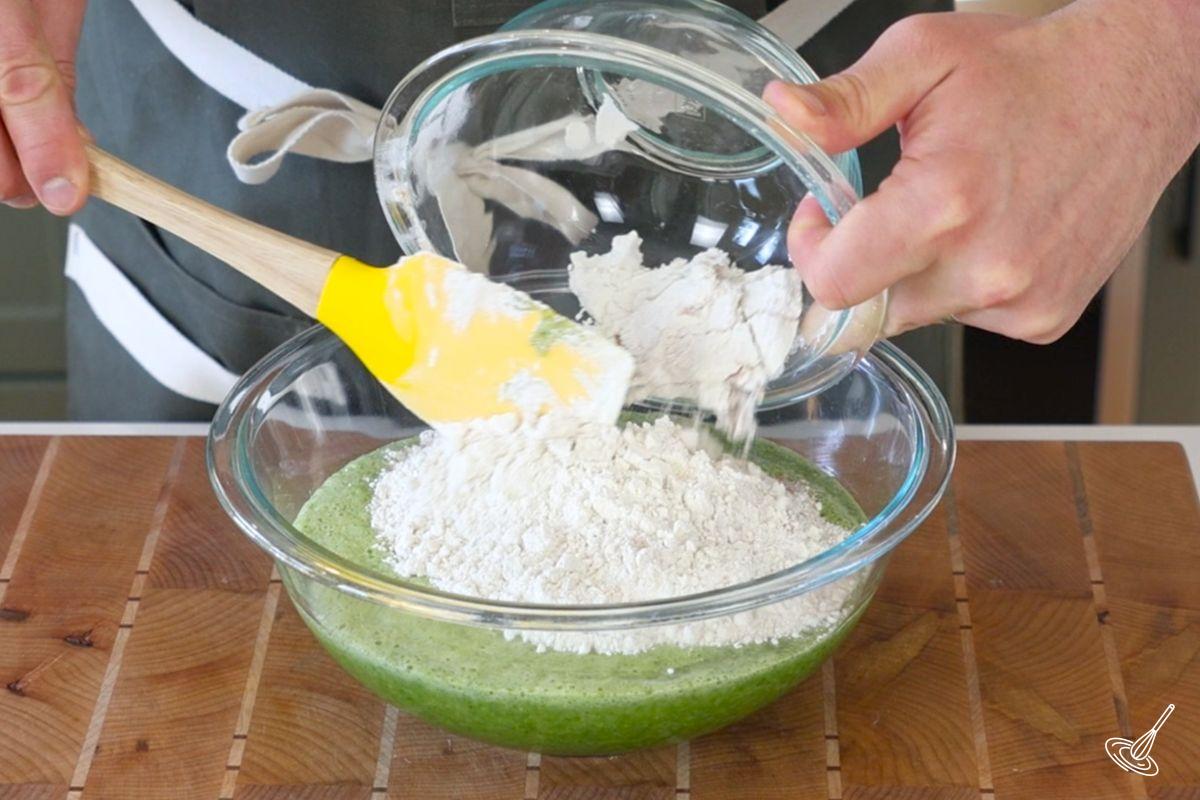 Someone adding a flour mixture to a large bowl of egg banana mixture. 