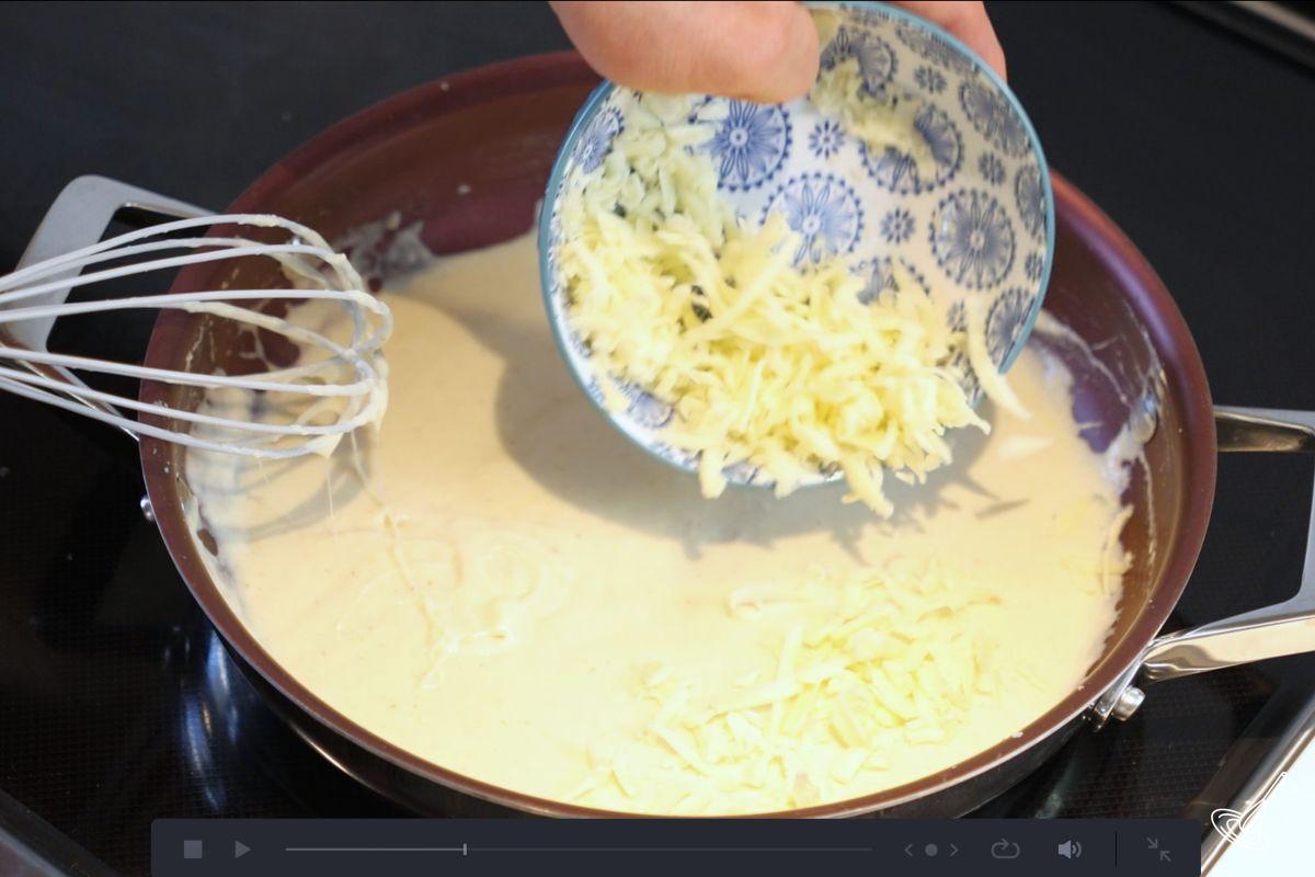 Someone whisking in grated cheese into a white sauce.