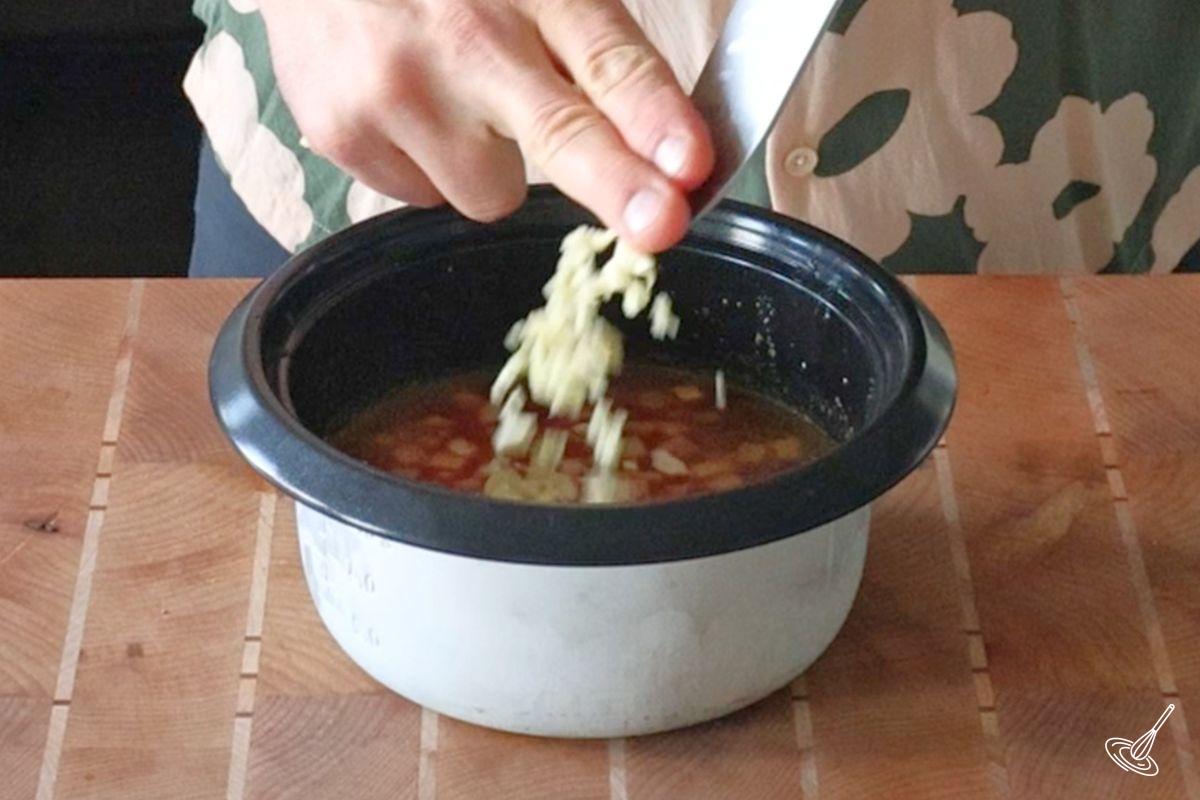 Someone adding minced garlic to the bowl of a rice cooker.