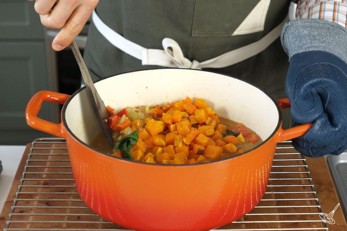 Someone stirring in roasted cubes of butternut squash in a pot of Golden Harvest soup.  