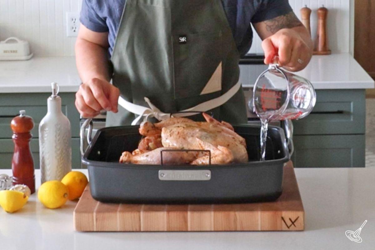 Someone pouring water in the bottom of a roaster pan. 