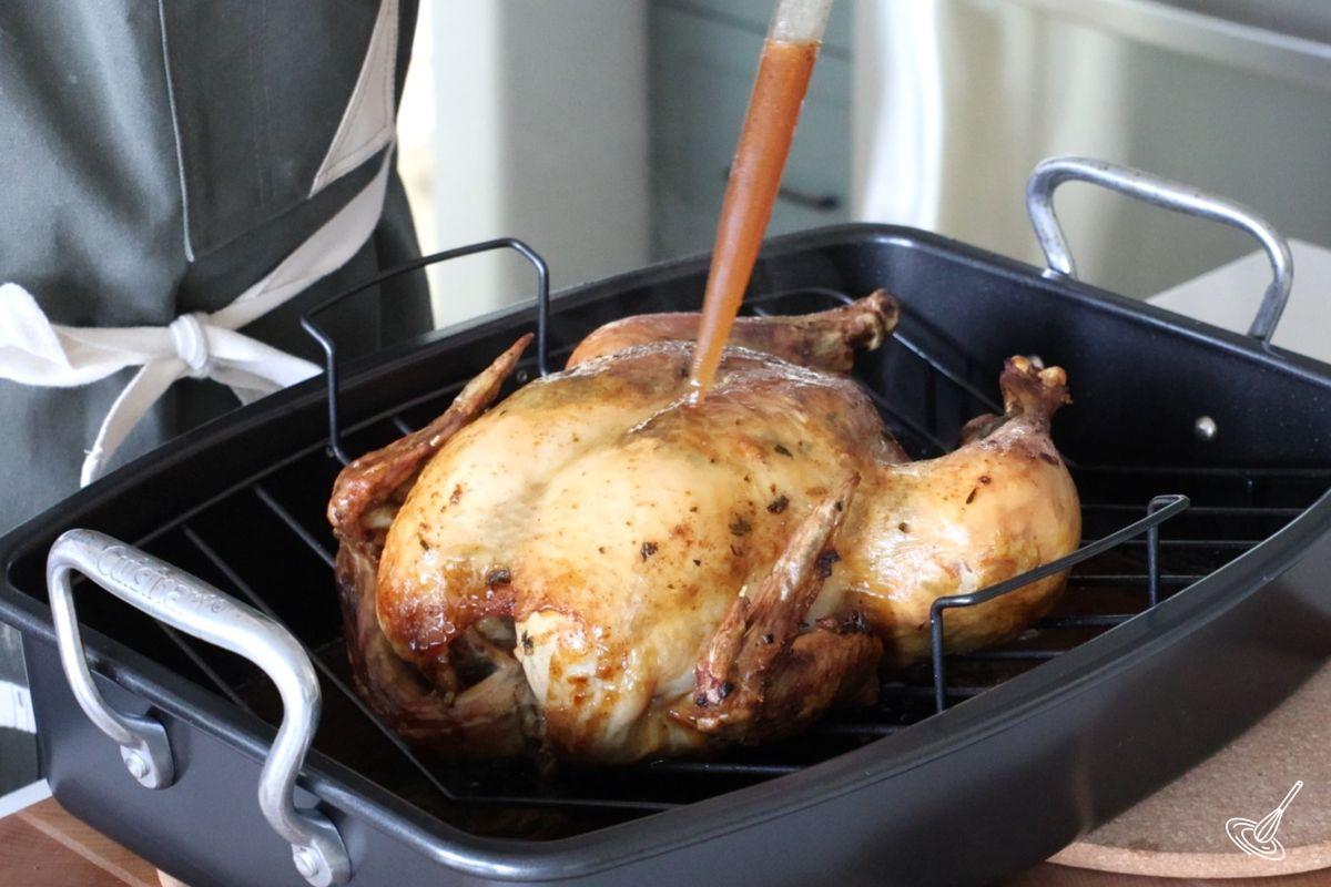 Someone basting a cooked Italian Roast Chiken. 