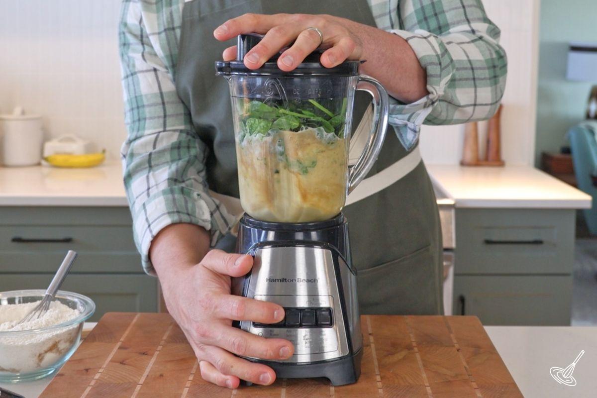 Someone using a blender to mix together wet ingredients to make the spinach banana muffins.