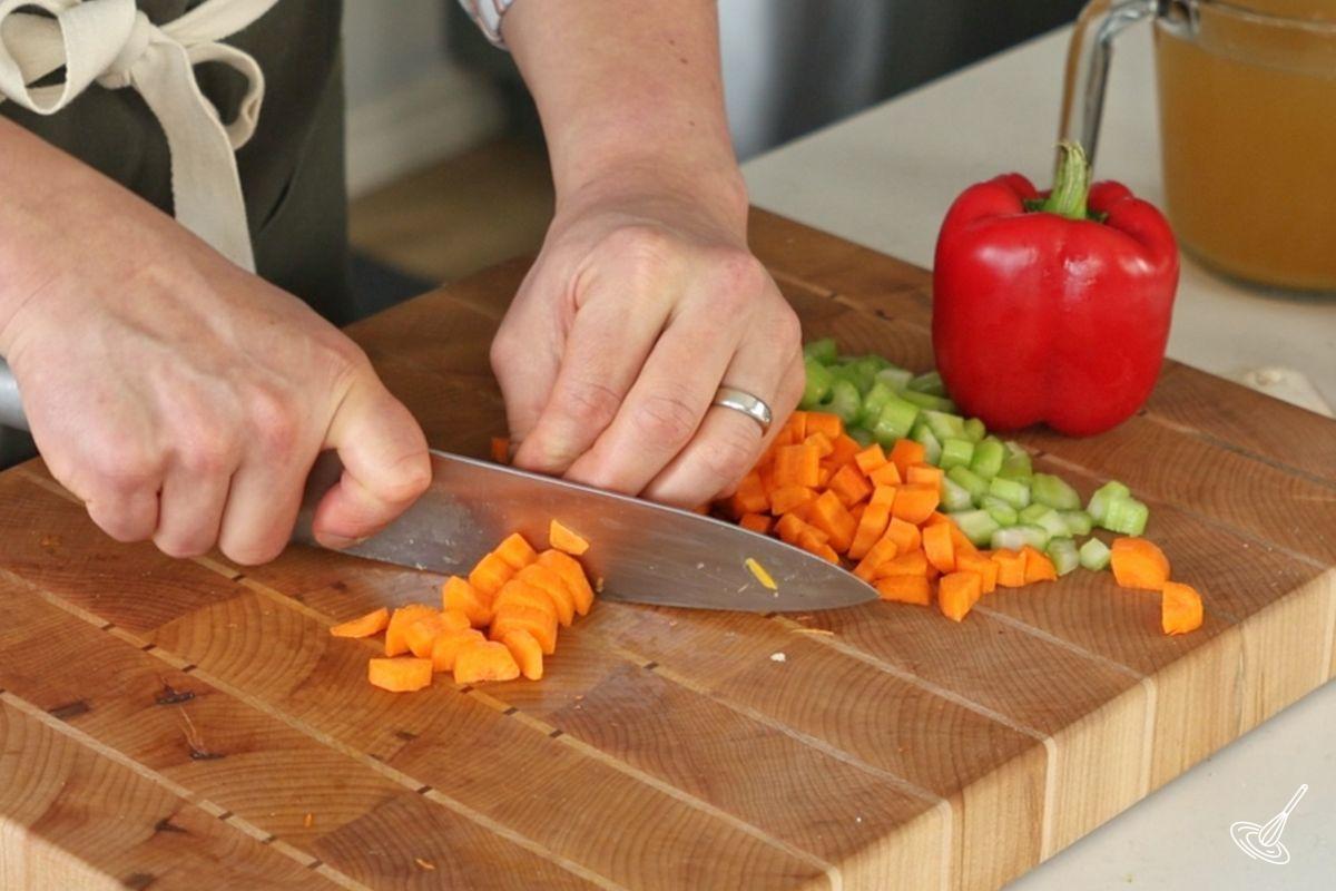 Someone using a knife to cut carrots in small pieces.