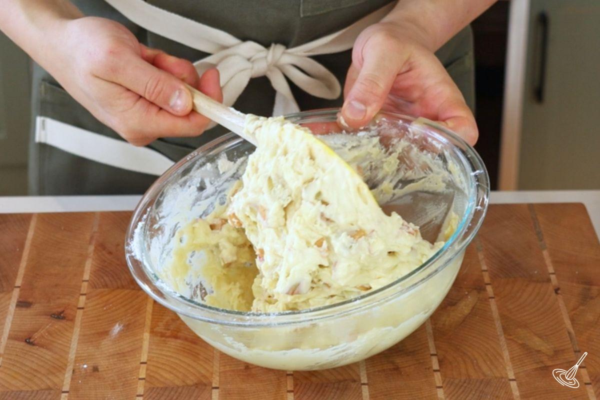 Someone using a rubber spatula to mix together apple coffee cake batter. 