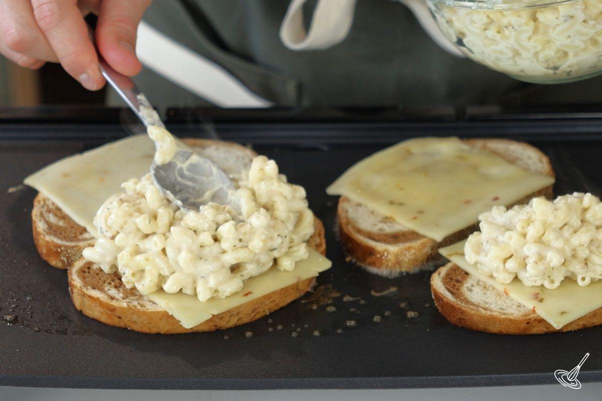 Someone assembling a mac n cheese grilled cheese on a griddle. 