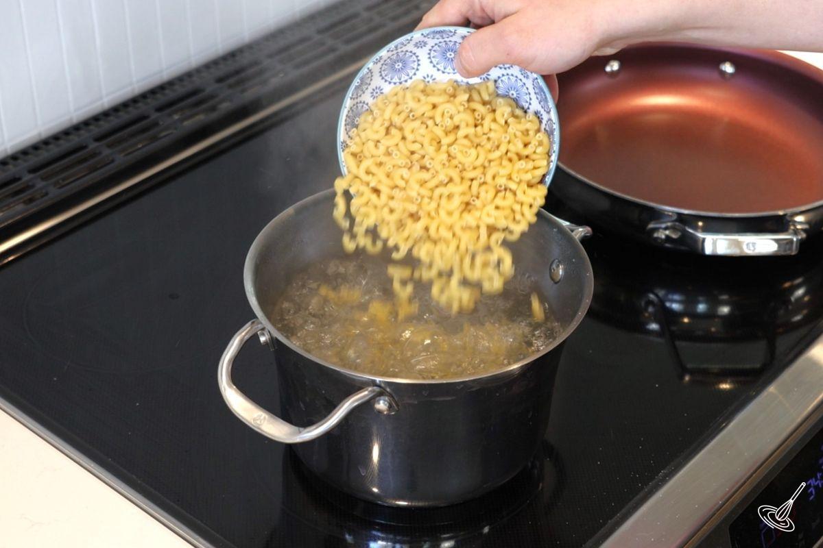 Someone adding macaroni pasta to a pot of boiling water. 