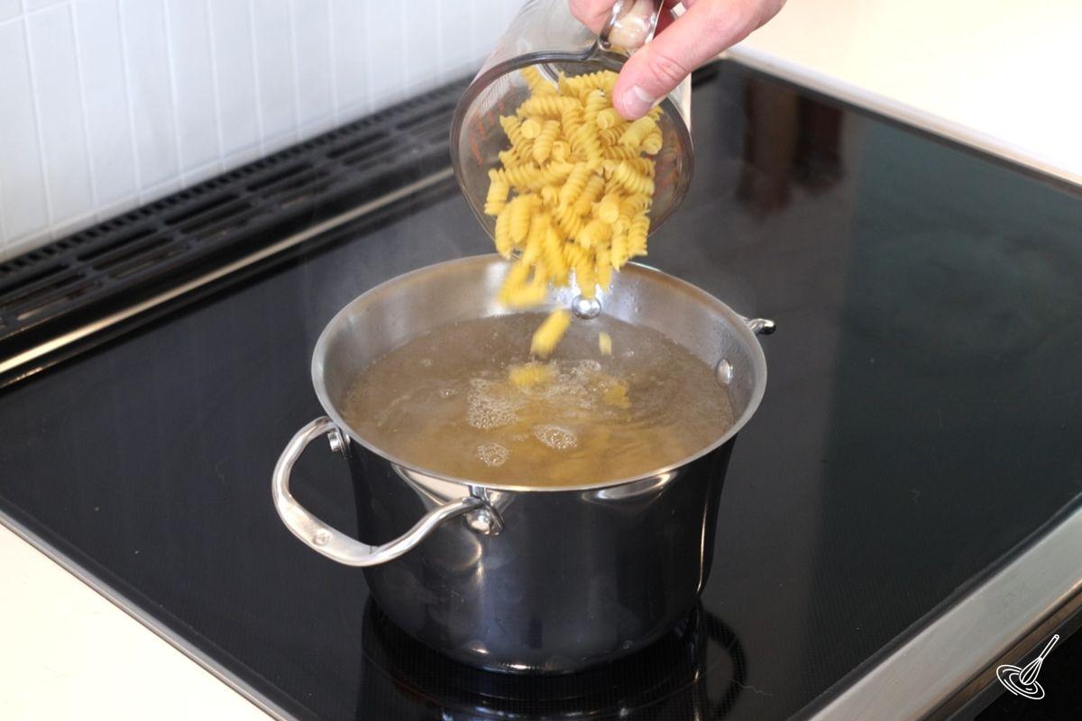 Someone pouring pasta into a pot of boiling water. 
