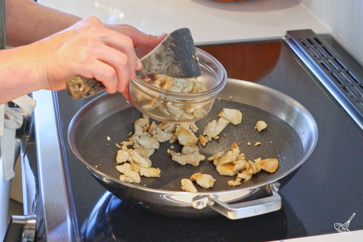 Someone taking cooked chicken out of a wok. 