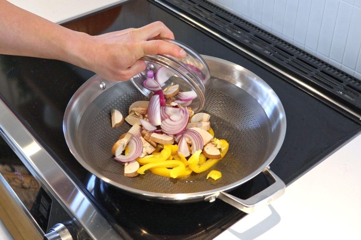 Someone adding sliced vegetables to a wok. 