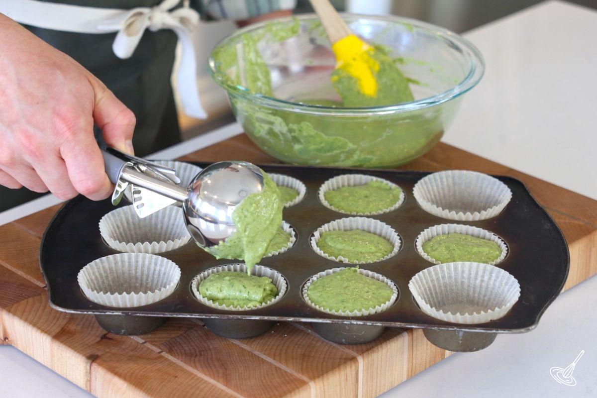Someone using a cookie scoop to divide the muffin batter in the muffin tin.