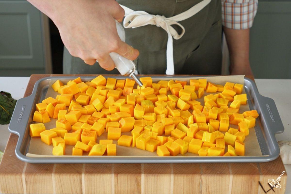 Someone drizzling olive oil over cubes of butternut squash.