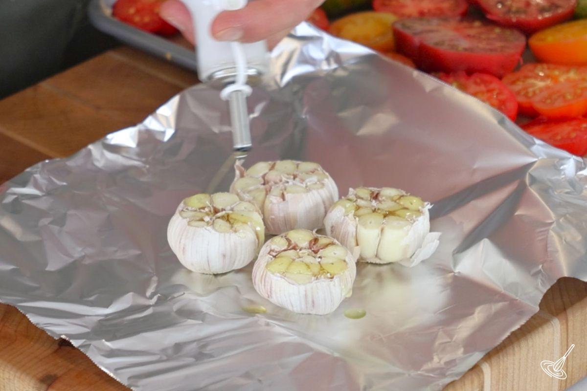 Someone drizzling olive oil on garlic bulbs. 
