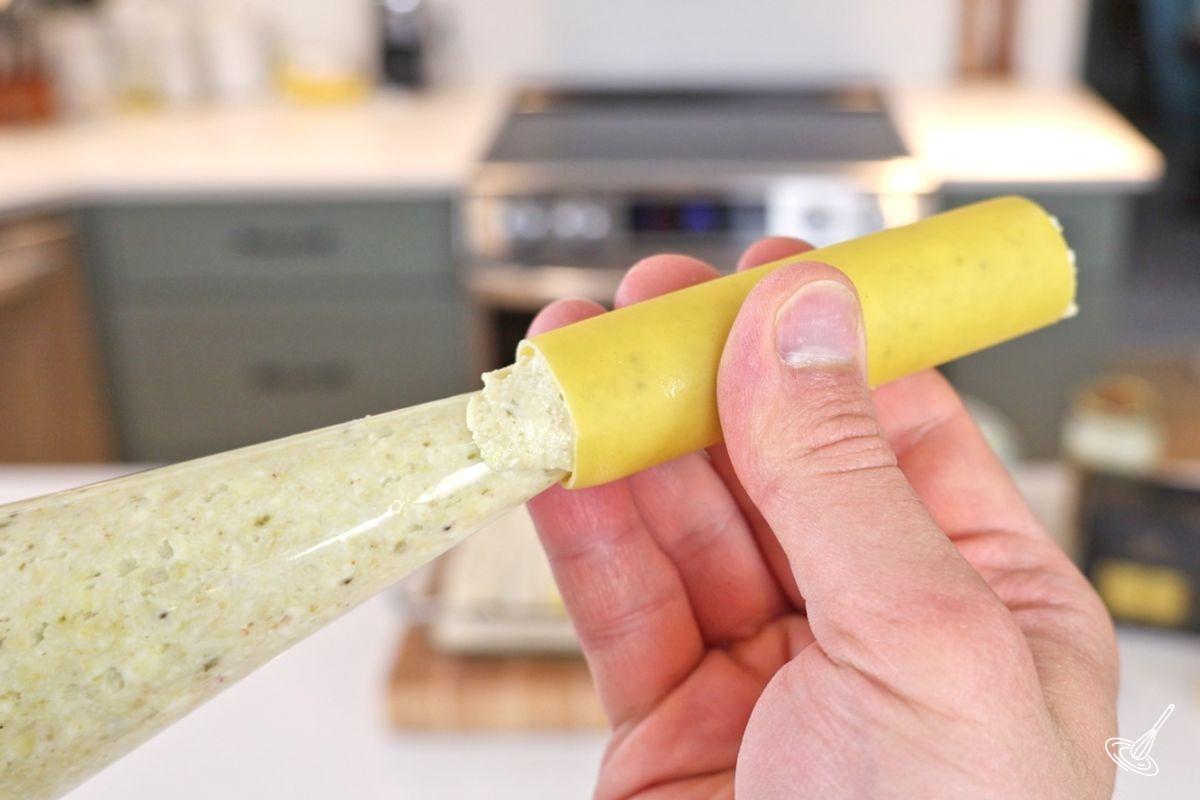 Someone using a piping back to fill a cannelloni.