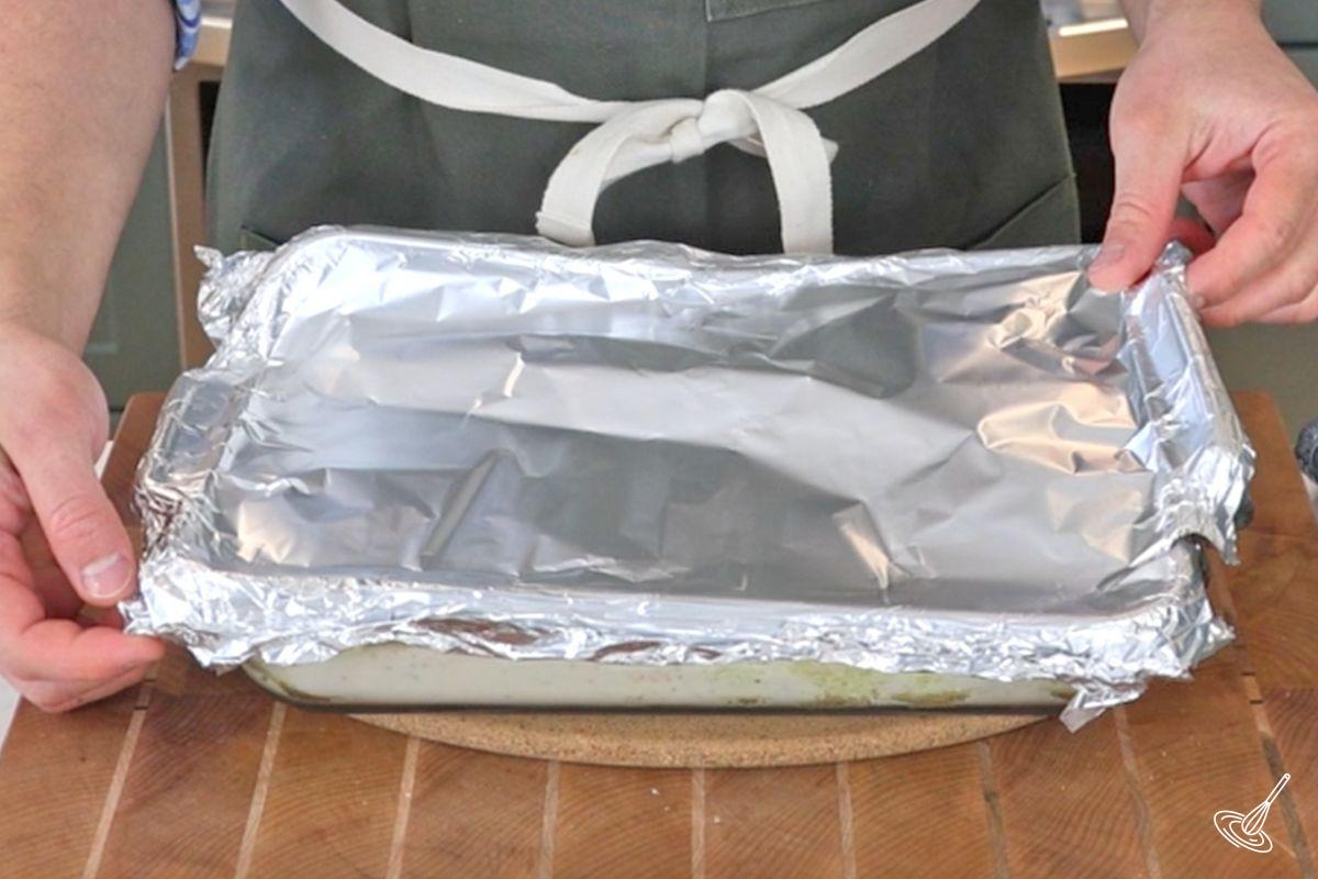 Someone covering a baking dish with aluminum foil.