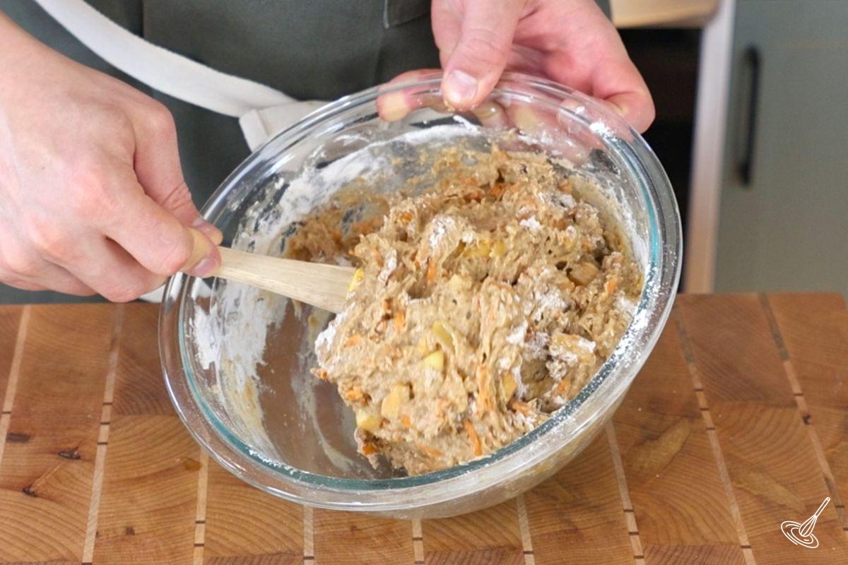Someone using a rubber spatula to mix together the batter for ABC Muffins. 