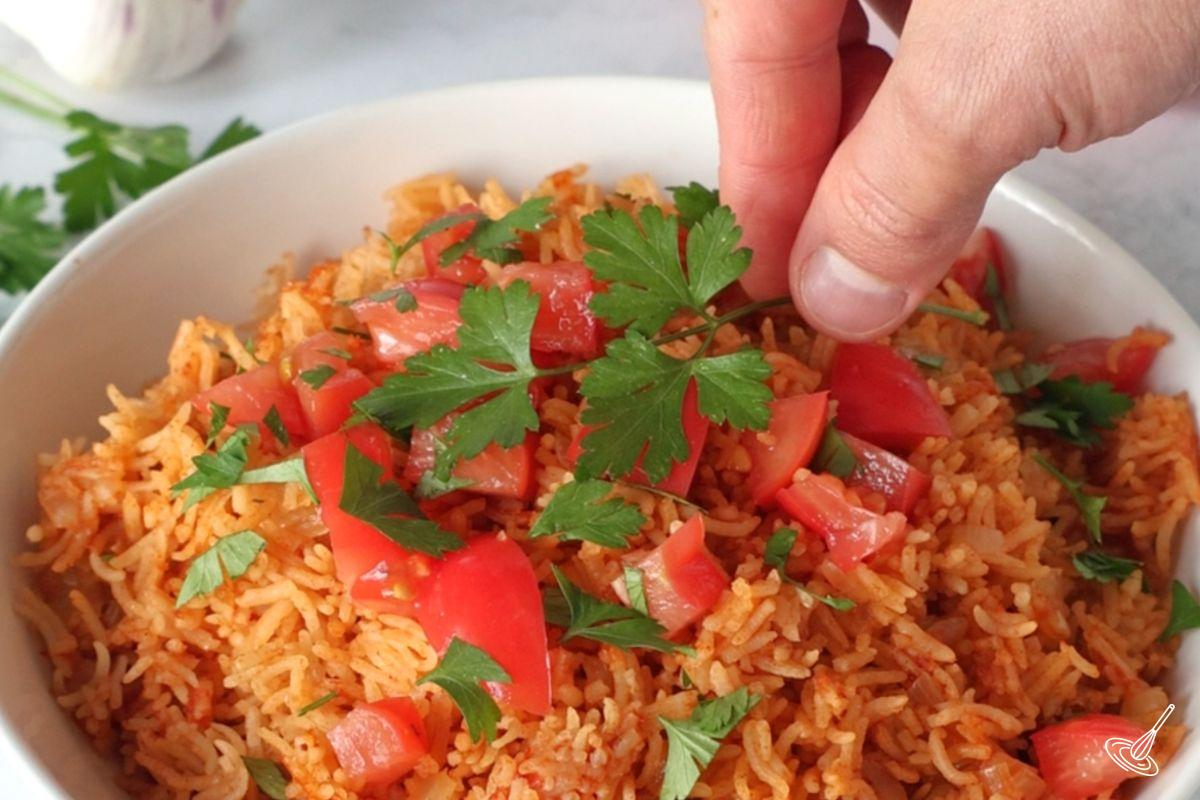 Someone placing a spring of cilantro on top of a bowl of Mexican rice. 