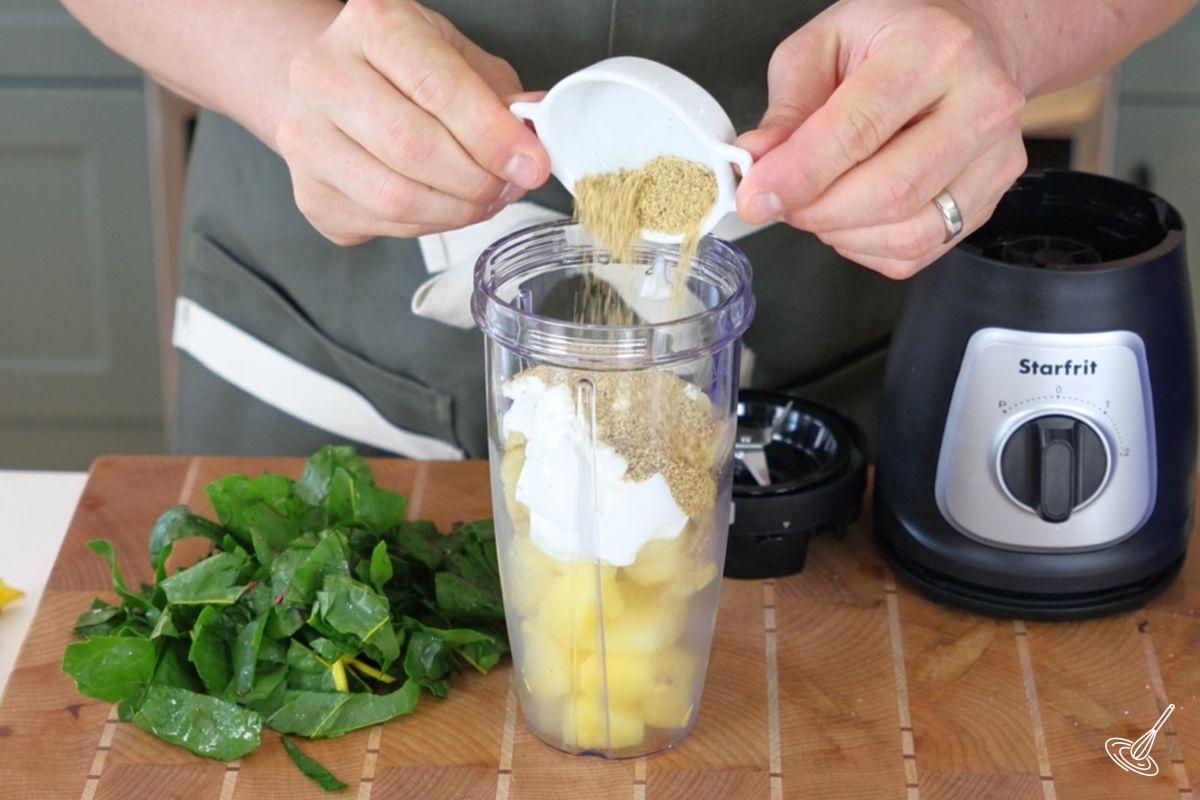 Someone adding ground flax seed to a blender jar with fruit. 