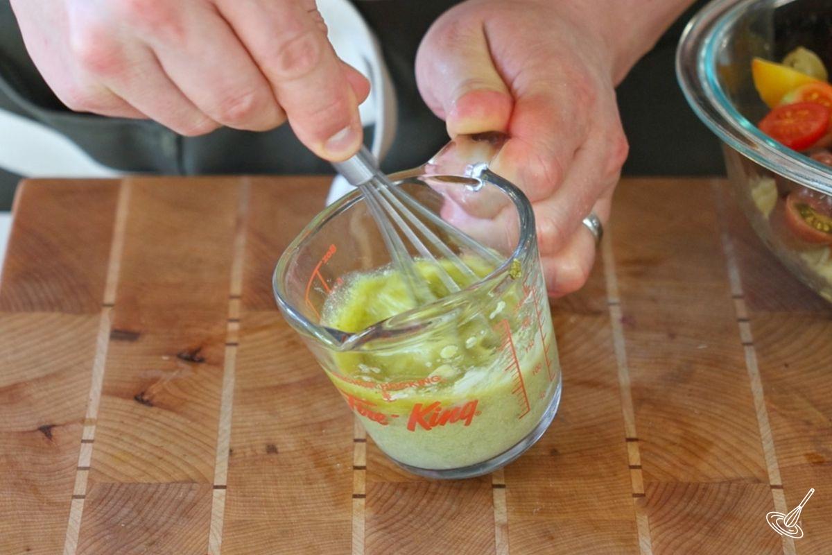 Someone whisking a measuring cup of green salad dressing.