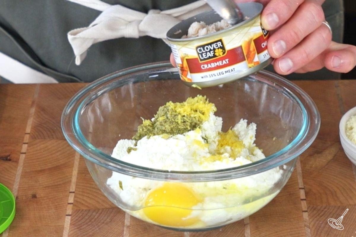 Someone adding a can of crab meat to a bowl of cannelloni filling.