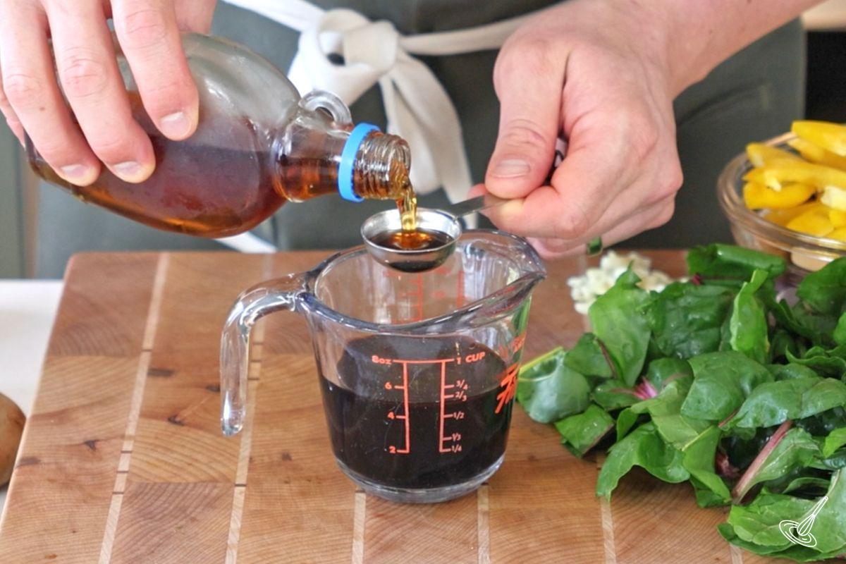 Someone adding maple syrup to a measuring cup of stir fry sauce. 
