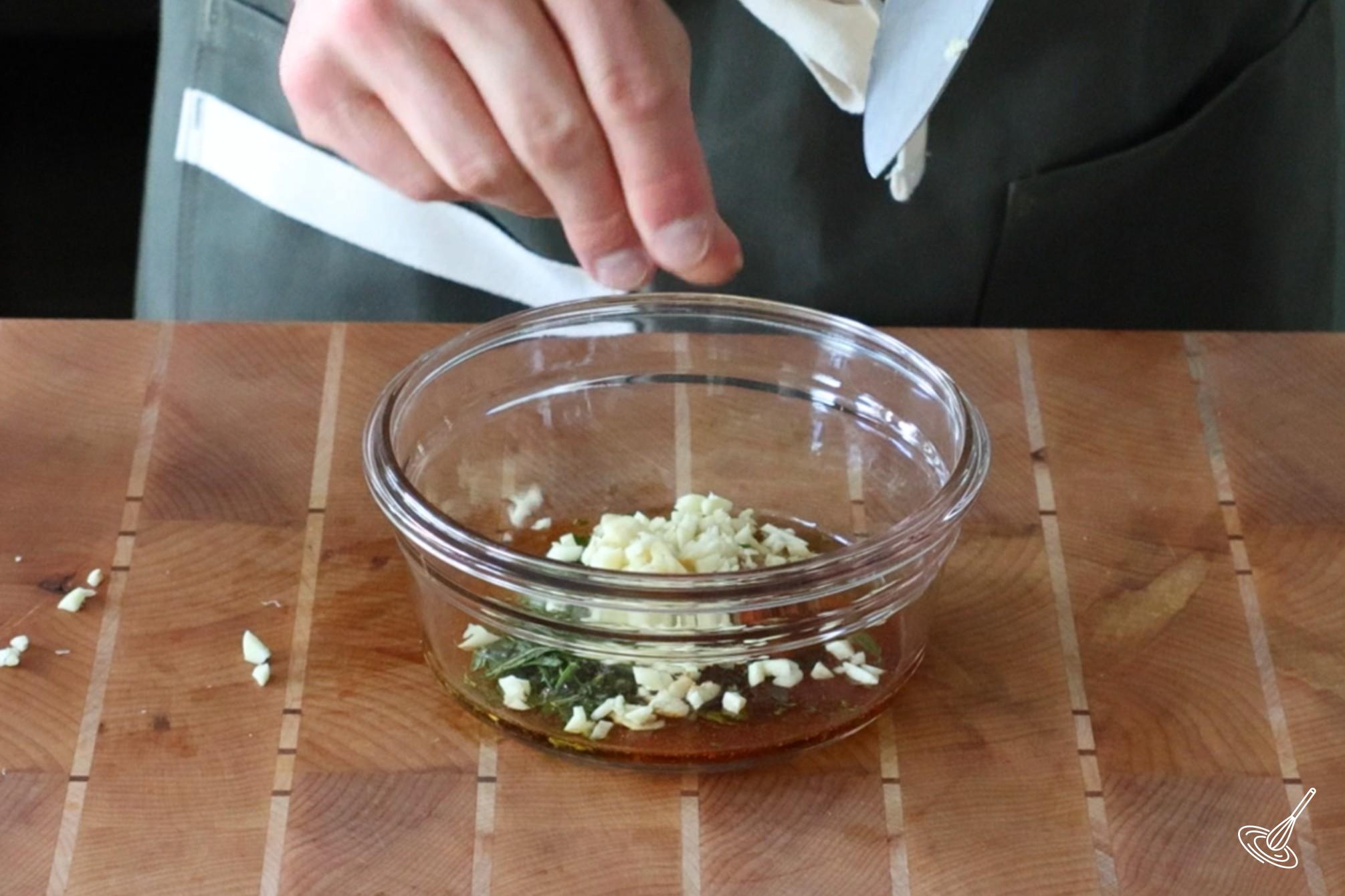Someone adding minced garlic to a small bowl of chicken rub.