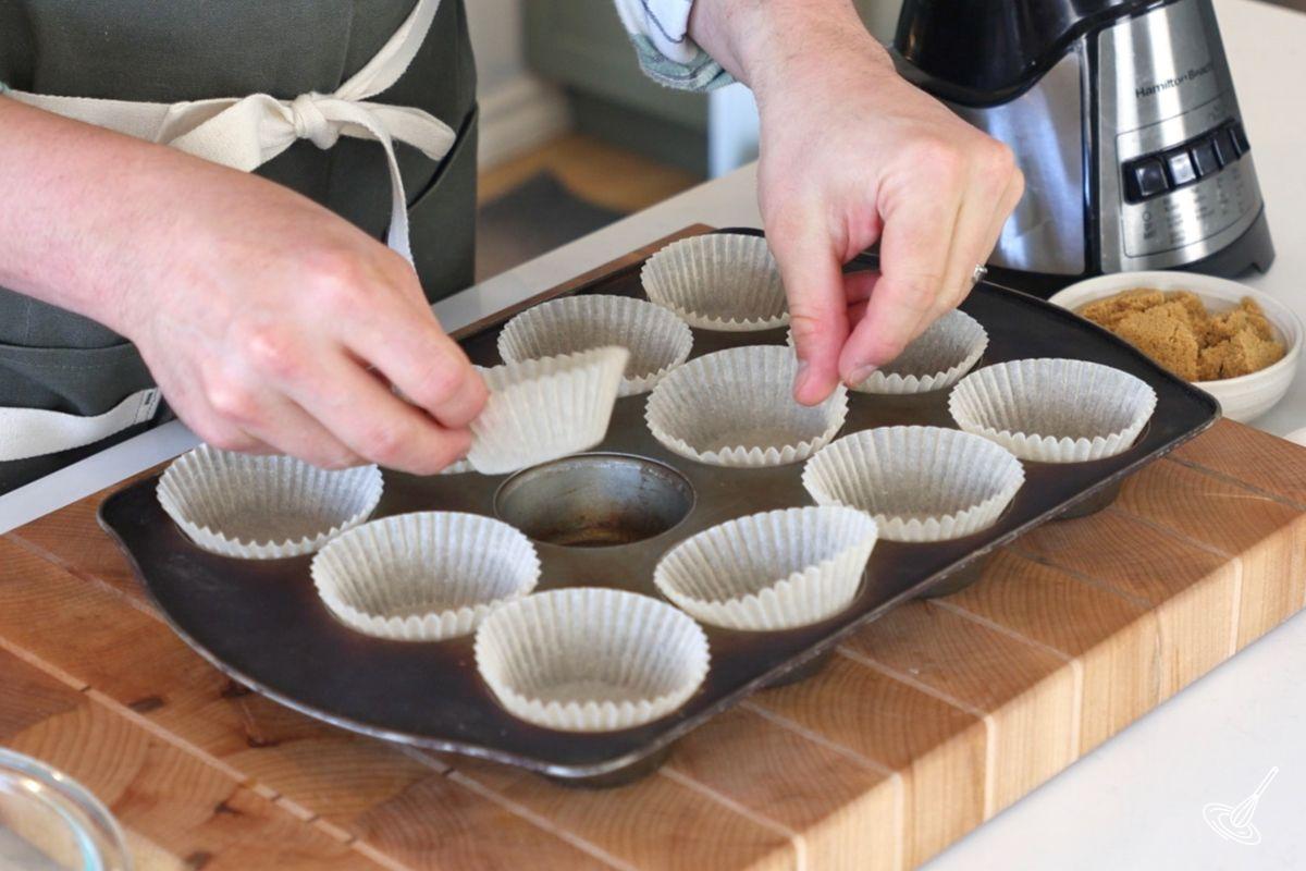 Someone placing muffin liners in a muffin pan.