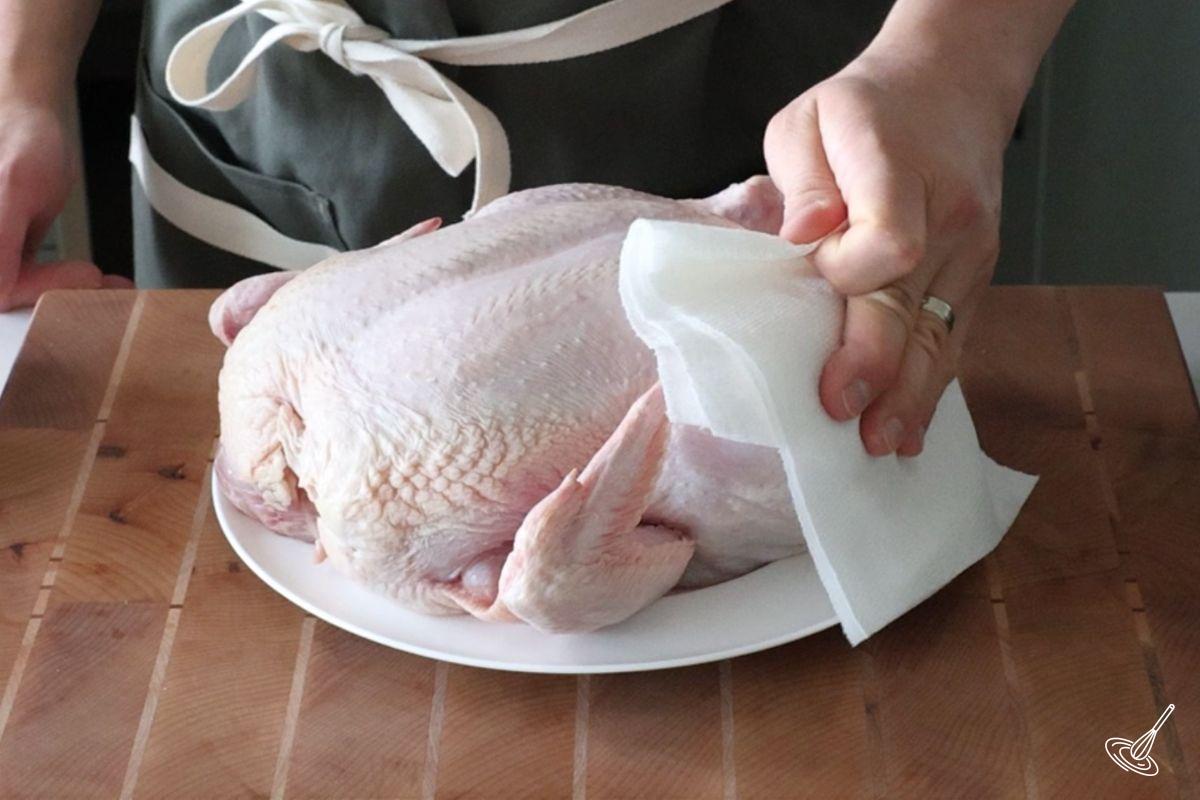 Someone using a paper towel to pat down a raw chicken. 
