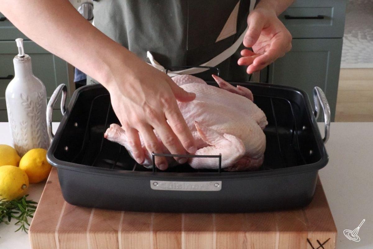 Someone placing a whole raw chicken inside of a roaster pan. 