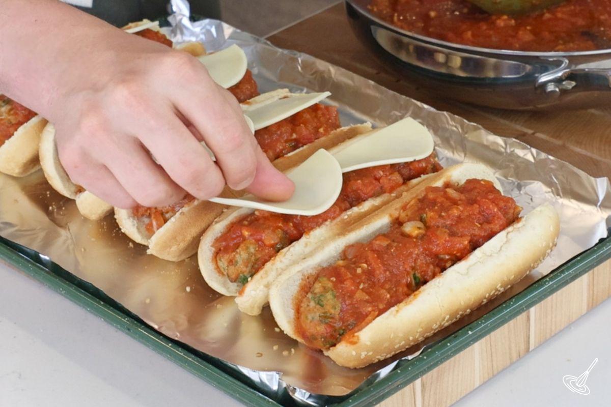 Someone placing slices of provolone cheese on top of turkey florentine meatball subs.