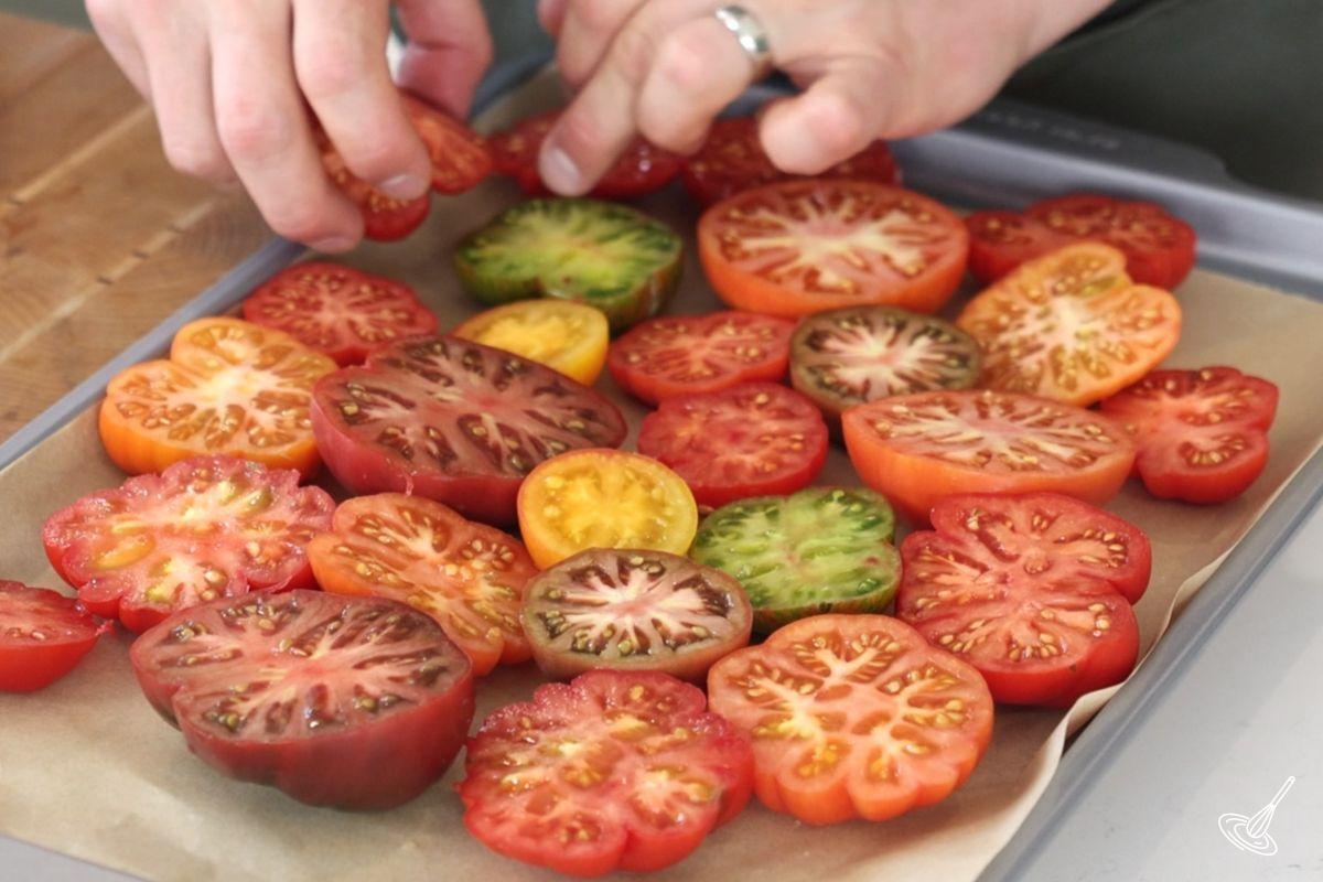 Halved tomatoes on a parchment paper lined baking tray.