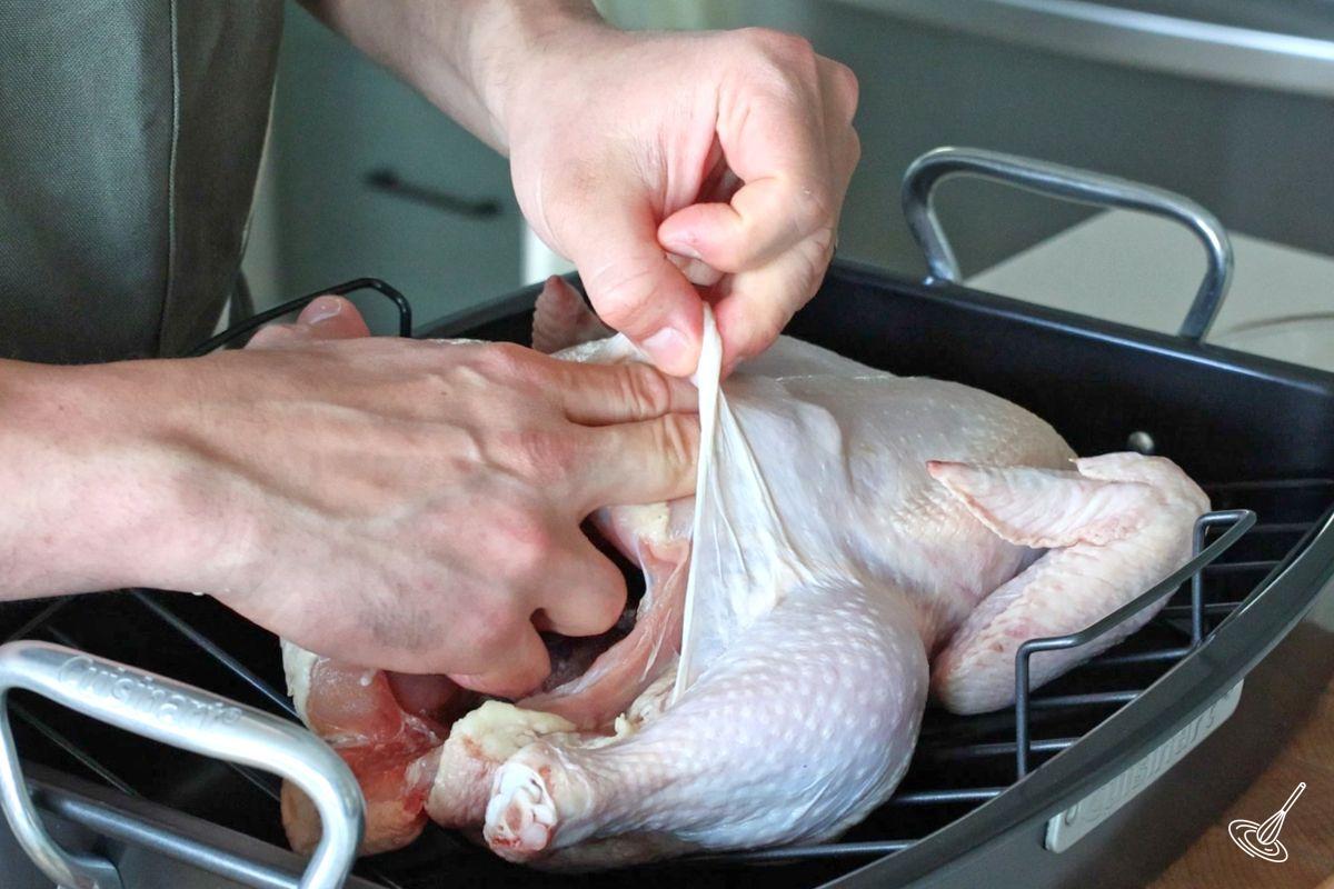 Someone separating the top skin of the chicken from the meat. 