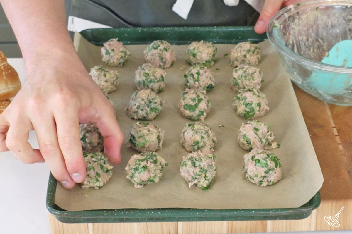 Someone placing turkey florentine meatballs on a baking pan. 