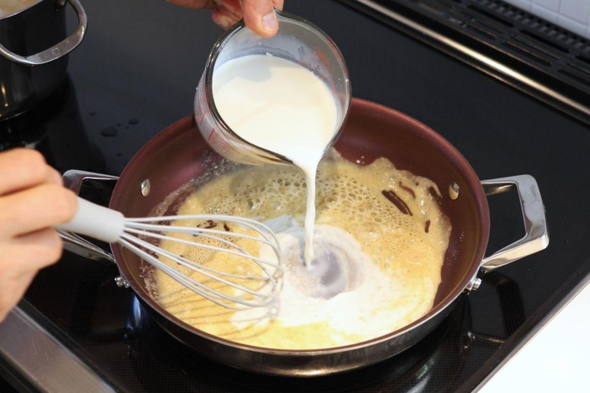 Someone whisking milk into a pan of roux. 