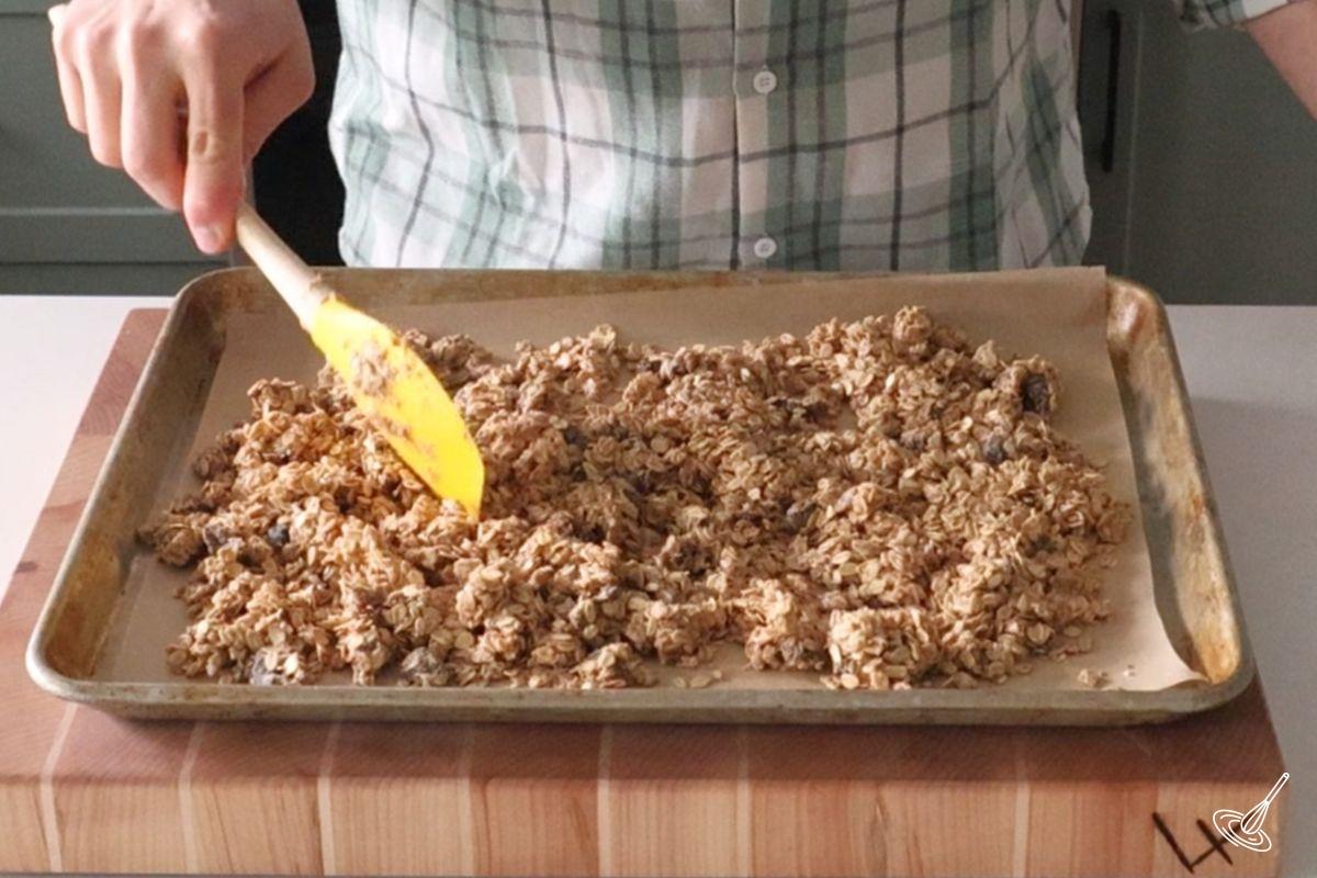 Someone using a rubber spatula to spread nut free granola on a baking sheet.