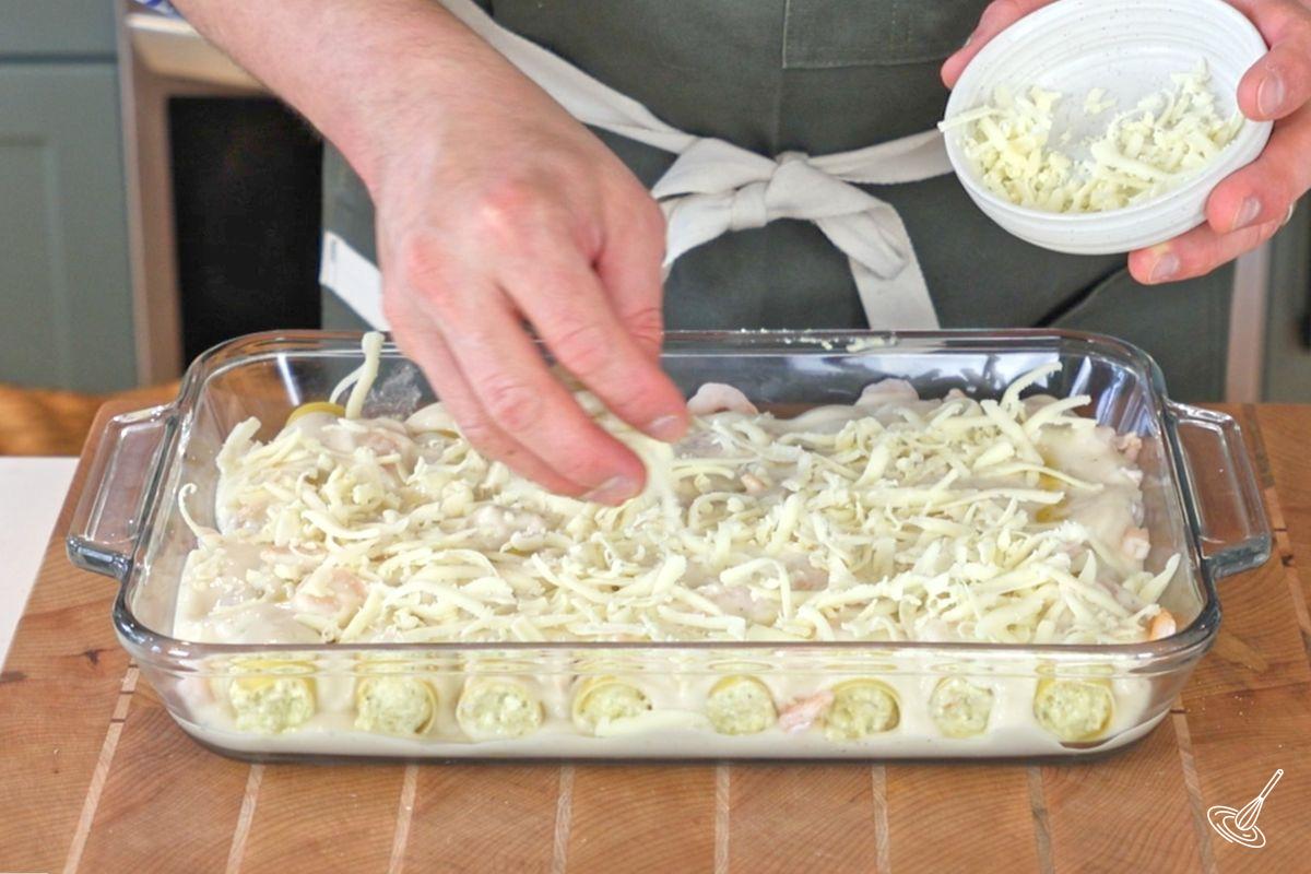 Someone sprinkling grates mozzarella over a dish of seafood cannellonis. 