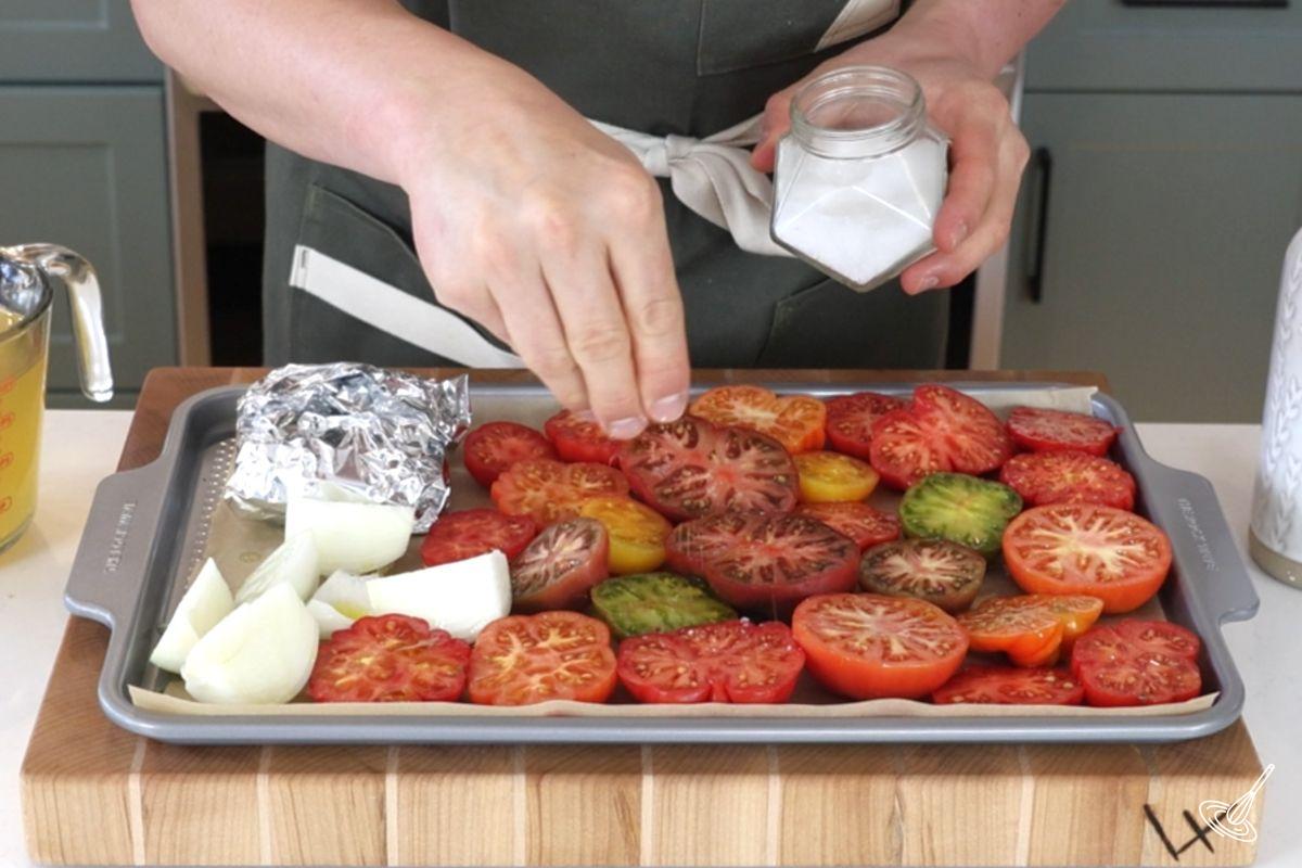 Someone sprinkling salt over a tray of tomatoes.