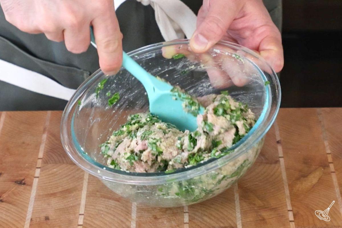 Someone using a rubber spatula to mix a bowl of turkey florentine meatball mixture.