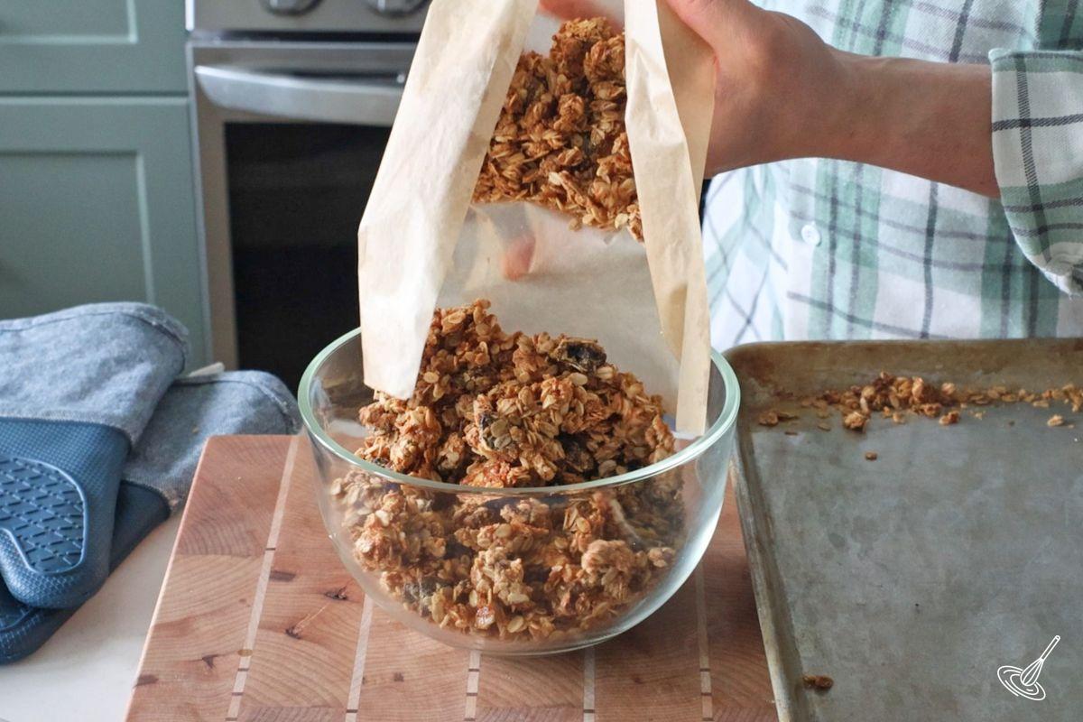 Someone placing cooked nut free granola in a glass storage container.