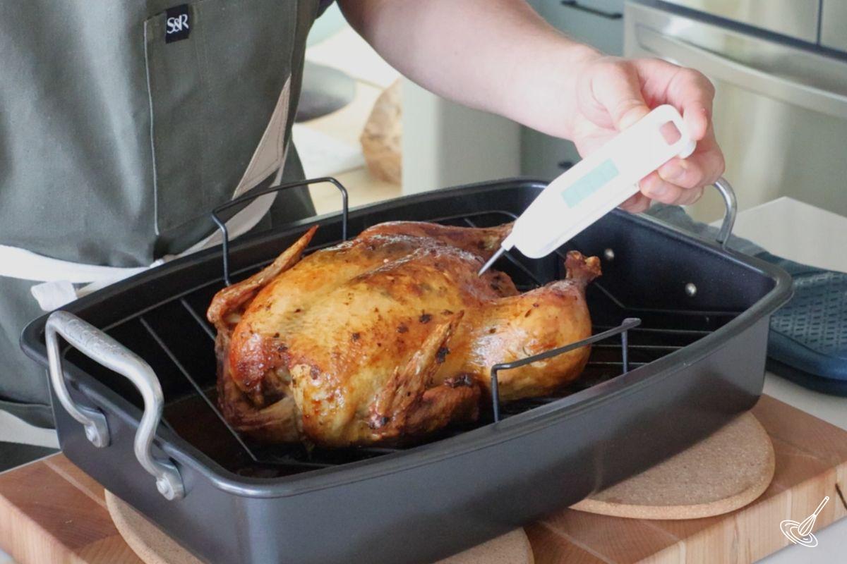 Someone using a digital probe thermometer to check the doneness of the roast chicken.