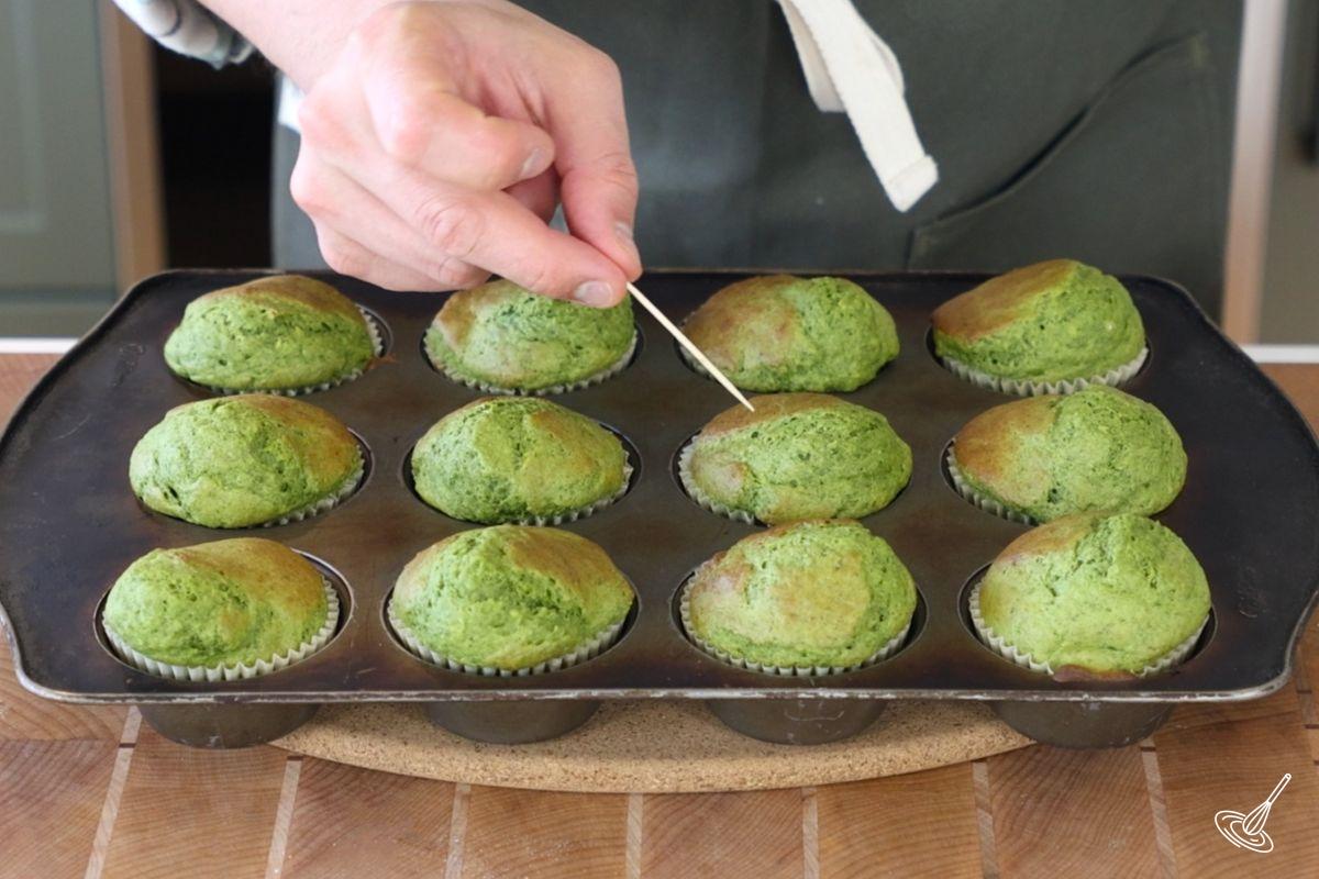 Someone using a toothpick to test the doneness of the spinach banana muffins.