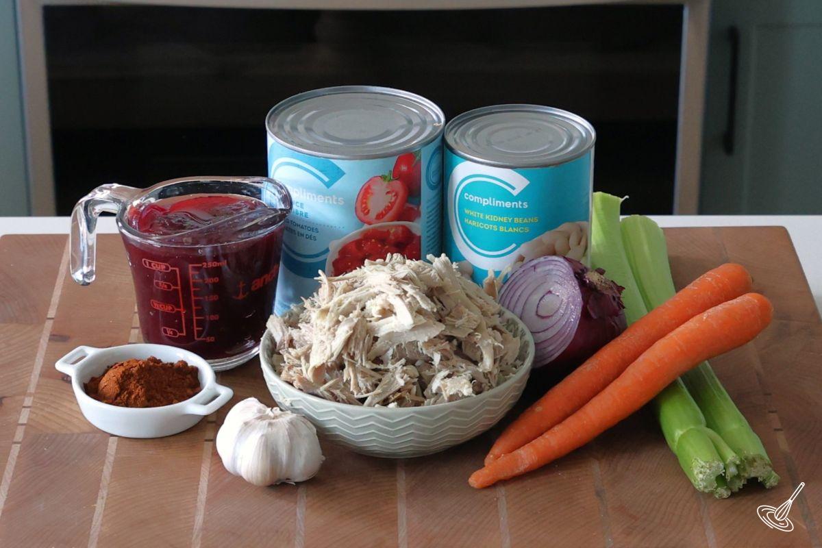 Ingredients on the counter to make Cranberry Turkey Chili, including shredded turkey, cranberry sauce, fresh vegetables, and canned beans. 